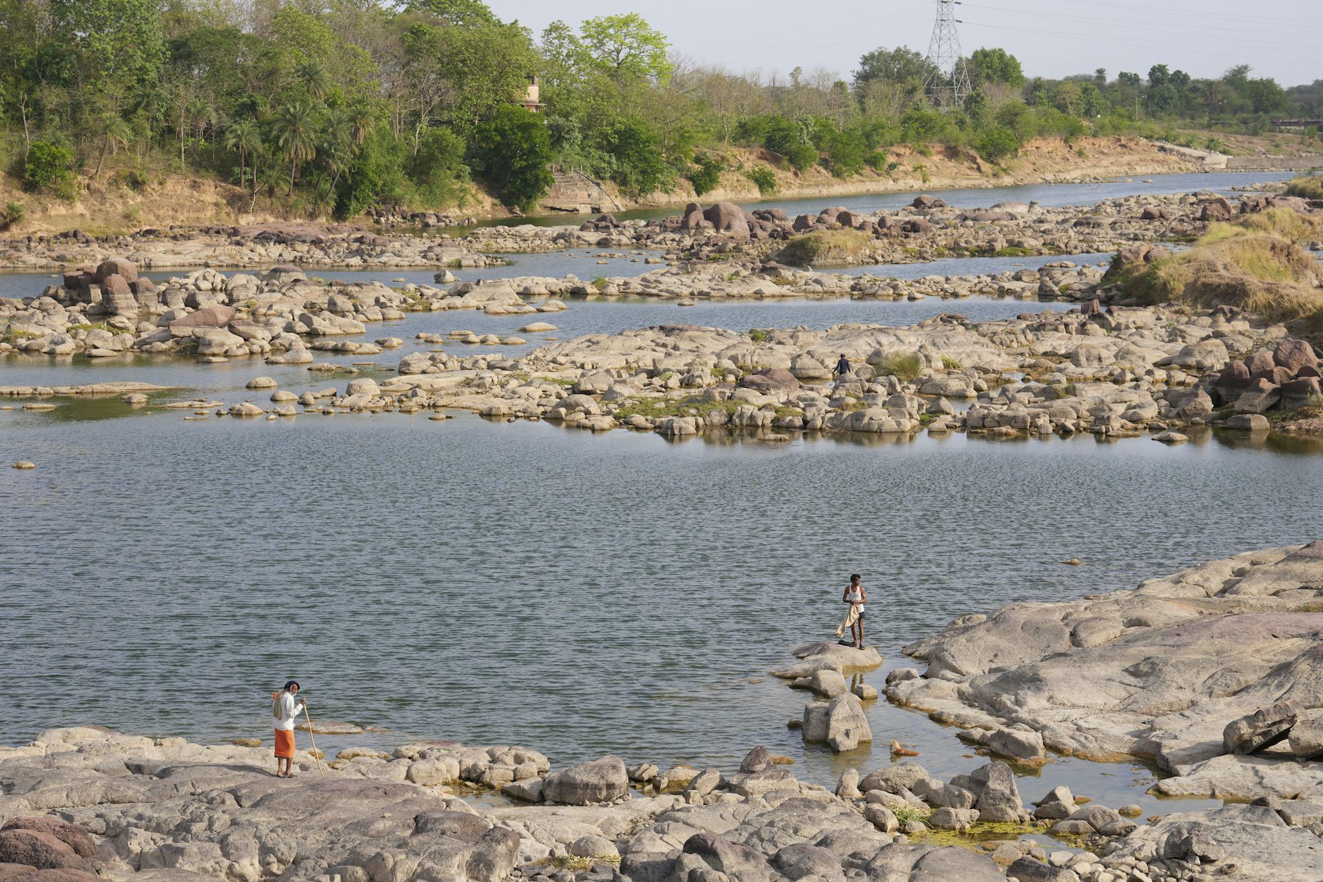 People stand on rocks next to shallow pools of water in a drying river bed.