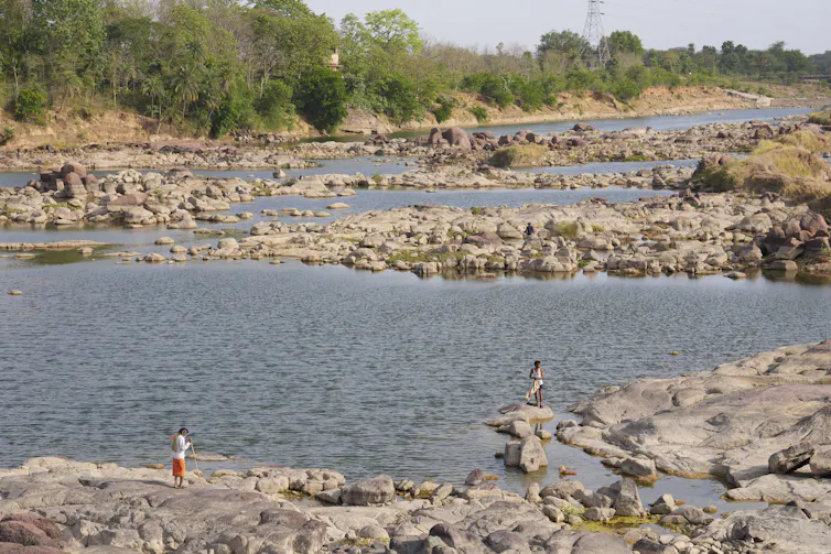 People stand on rocks next to shallow pools of water in a drying river bed.