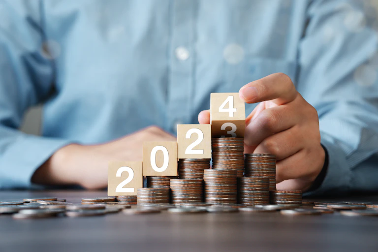 Several piles of coins are lined up on a table. On top of the piles are several wooden cubes; together they read "2024."