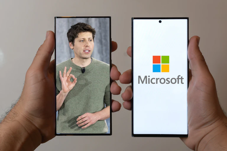 Two hands holding smarphones, one with an image of Sam Altman, the other with a Microsoft logo.