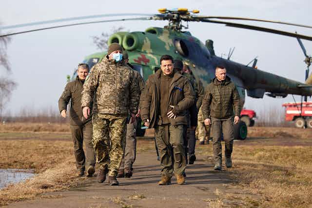President Zelensky in khaki ahead of some soldiers and a helicopter