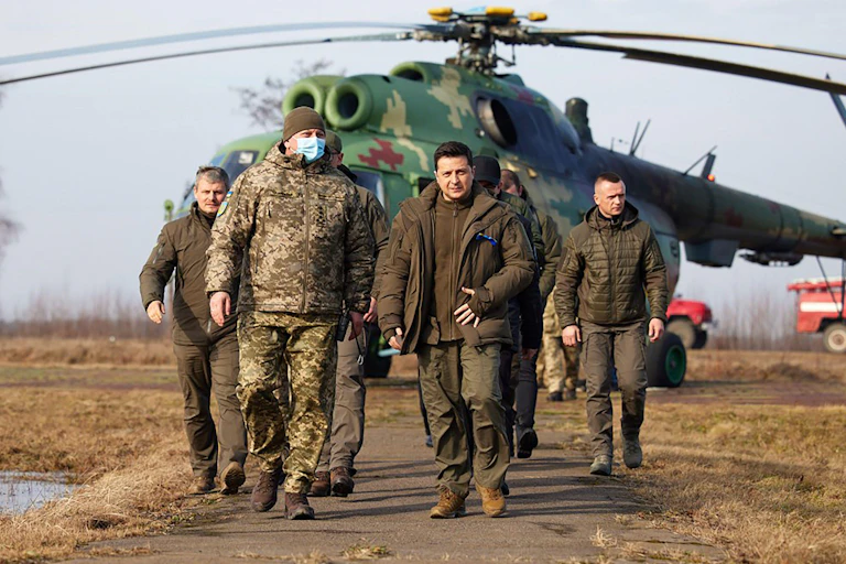 President Zelensky in khaki ahead of some soldiers and a helicopter