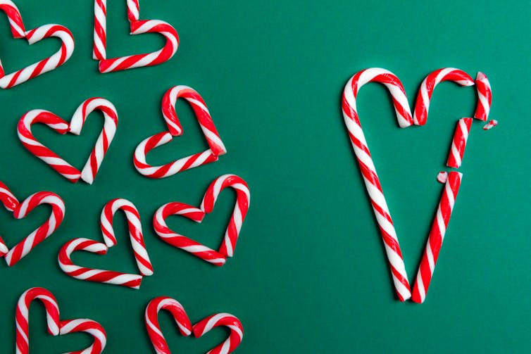 Red and white mini candy canes arranged in a heart shape and large candy canes in a heart shape with one side broken into three pieces.