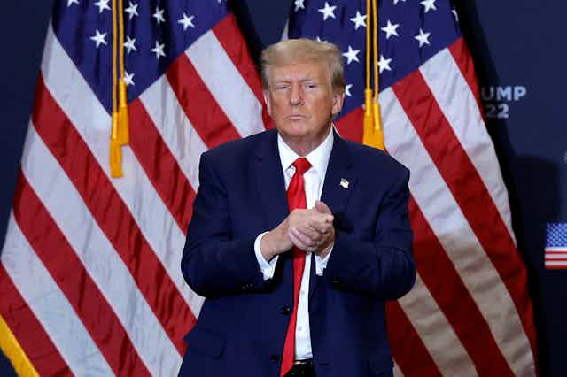 A man standing in front of two American flags, dressed in red, white and blue.