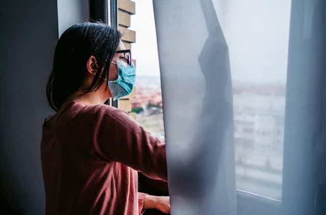 woman in mask looking out a window