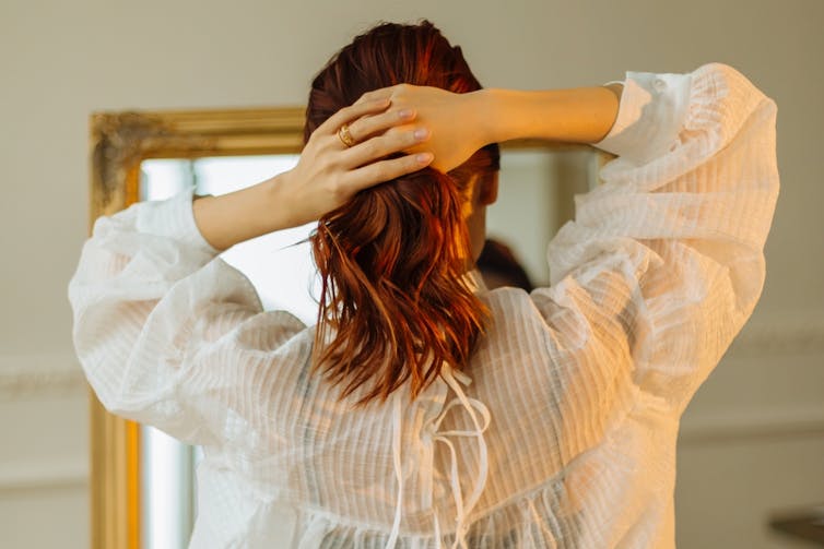 A woman with wavy hair looks in a mirror