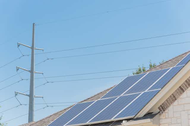Transmission lines behind a house roof with solar panels