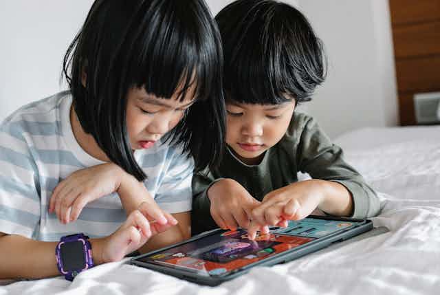 Two small children play on a tablet together. 