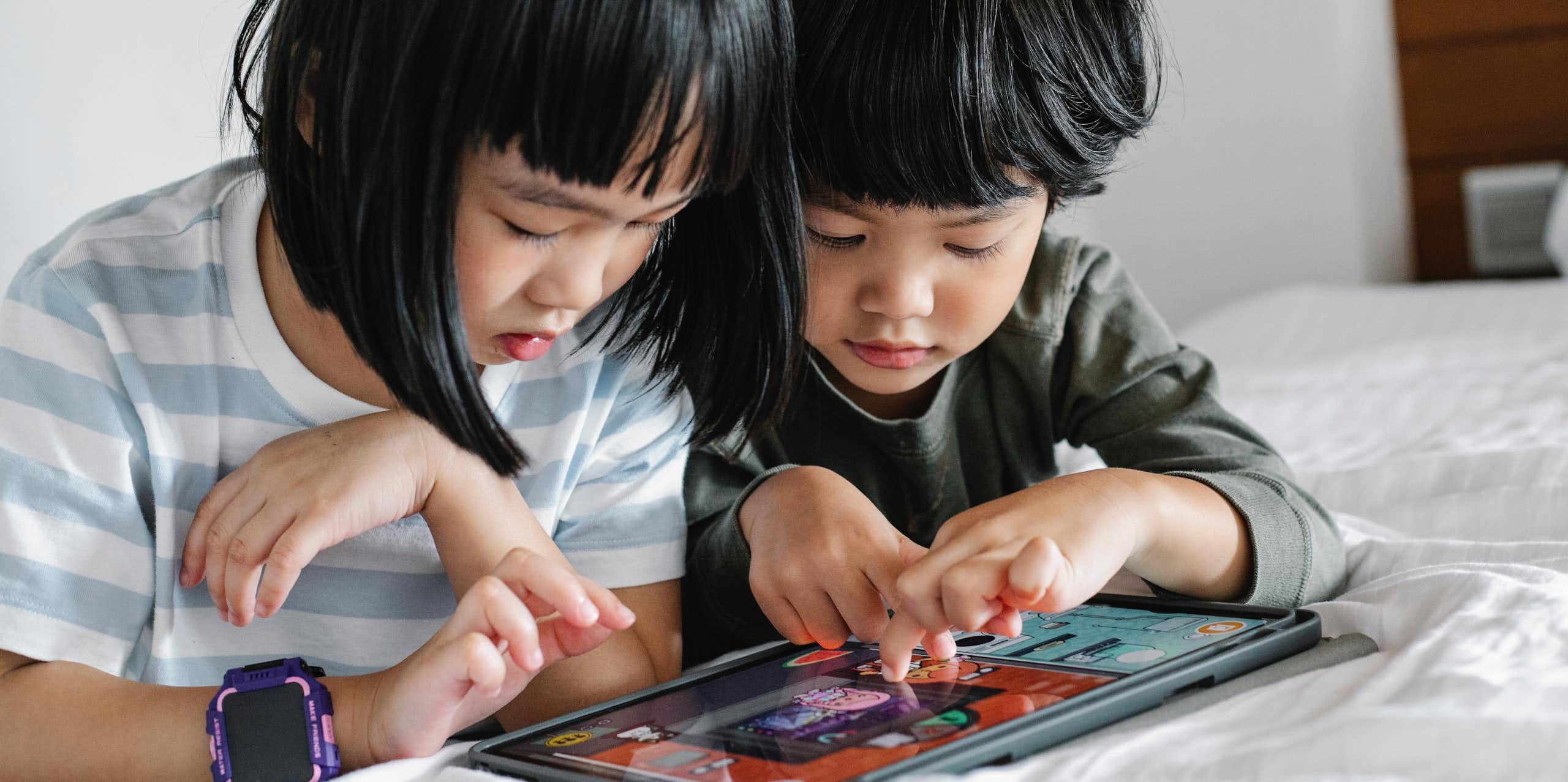 Two small children play on a tablet together. 