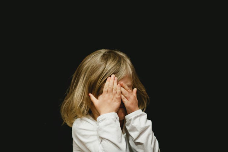 A young girl covers her face with her hands.