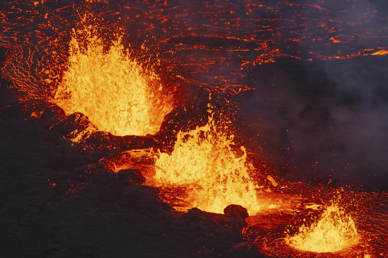 Glowing lava erupts through a series of ruptures, and flows out a glowing fan pattern.