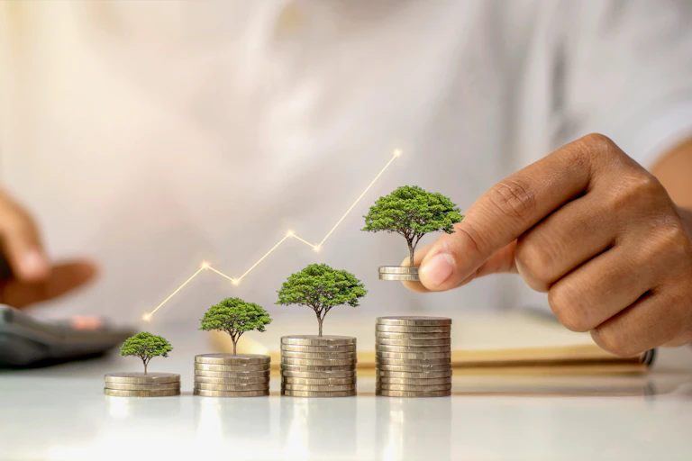A businessman holding a coin with a tree growing on a pile of money.