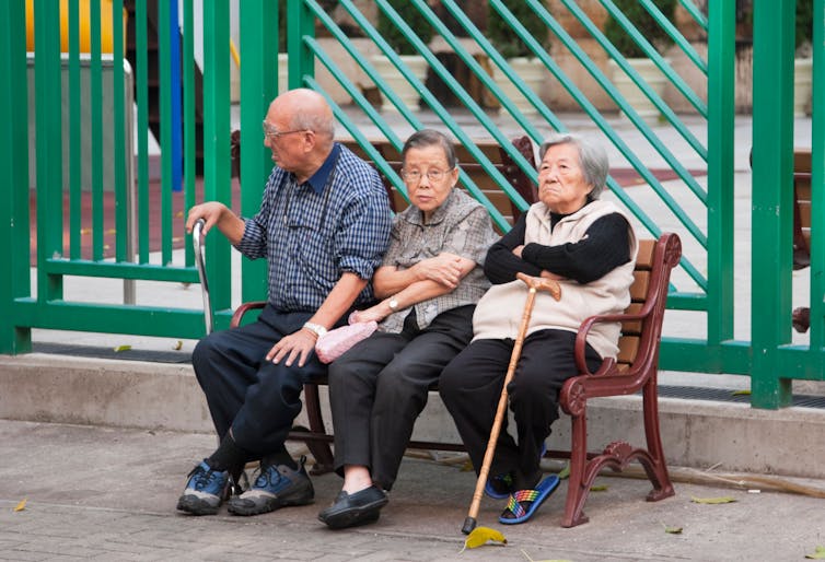 Three older people sit on a bench.