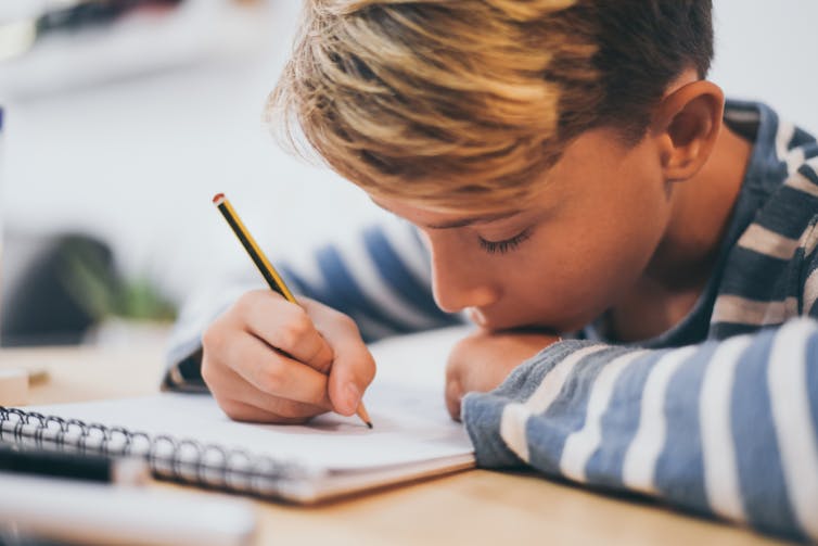 Boy writing in notebook with pencil