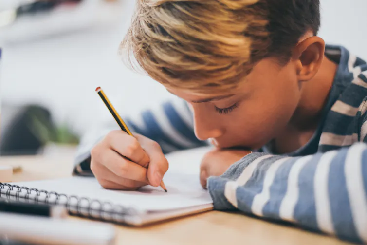 Boy writing in notebook with pencil