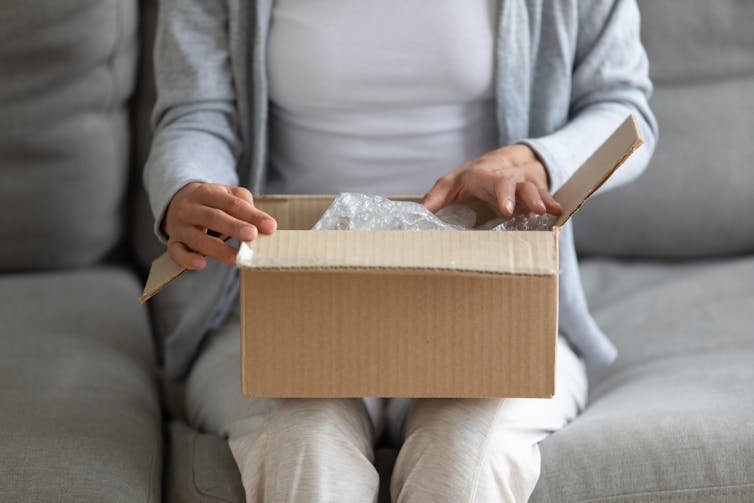 A woman opening a box, which sits on her lap.