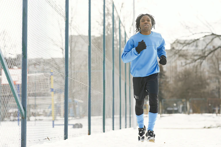 A man in a blue sweatshirt running beside a fence in winter