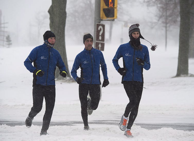 Three runners in blue jackets on a snowy road