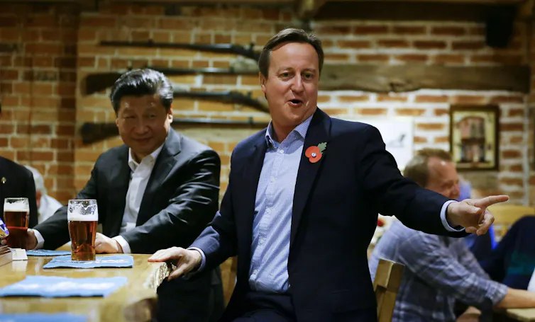 David Cameron and Xi Jinping standing at the bar in a pub with pints of beer.