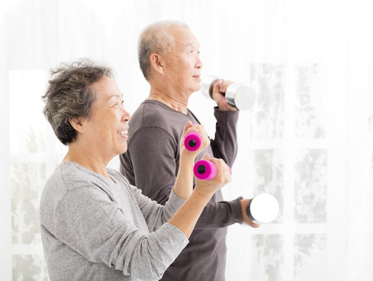 An older couple in sweatshirts using small dumbbells
