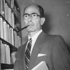 Retrato contrapicado de un hombre mayor con gafas y calvo, que fuma en pipa.