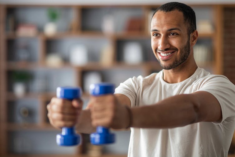 A smiling man holding small blue dumbbells