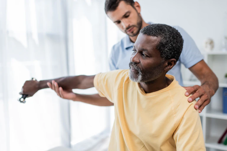 A man with a physiotherapist, helping him lift a small dumbbell with one arm