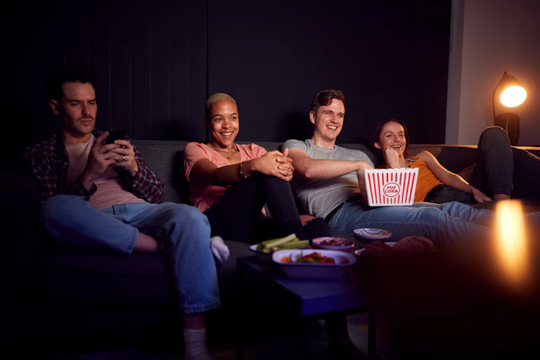 Un grupo de amigos ve la televisión mientras uno de ellos consulta el teléfono móvil.