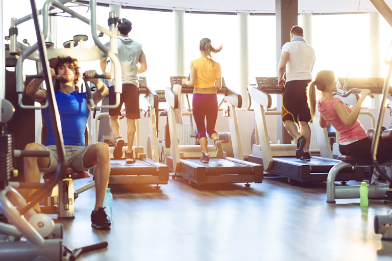 people on treadmills and using weight machines at a gym
