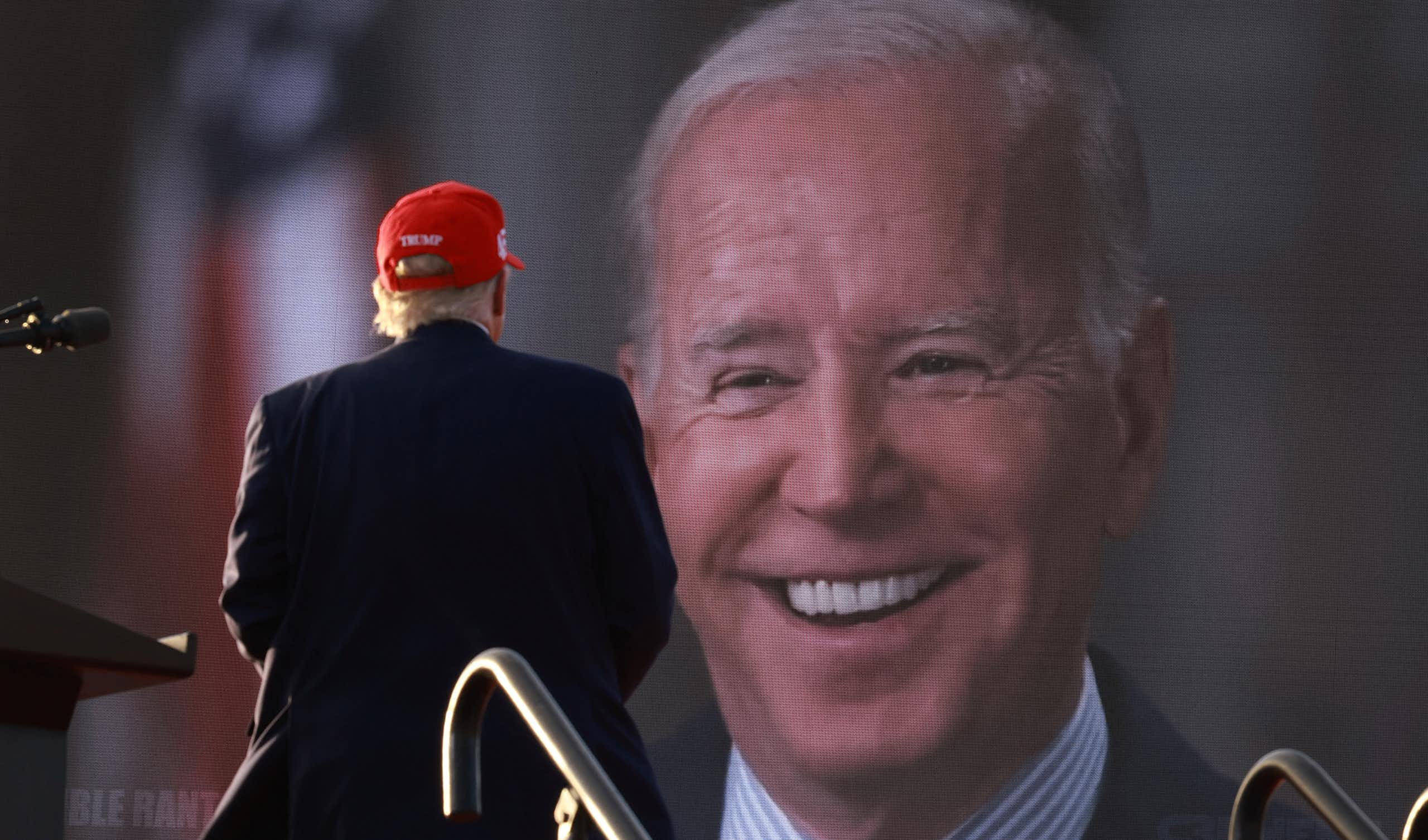 Donald Trump, de dos, pendant un meeting, regarde un écran géant sur lequel on voit Joe Biden.