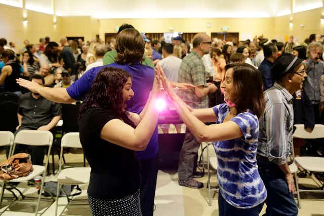 Two women high-five each other in a room full of folding chairs and standing people.