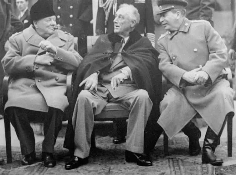 A black-and-white photo shows three men in overcoats talking.