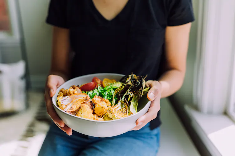 A woman holding a bowl of vegetarian or vegan foods.