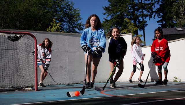 Young teen girls seen playing ballhockey outdoors.
