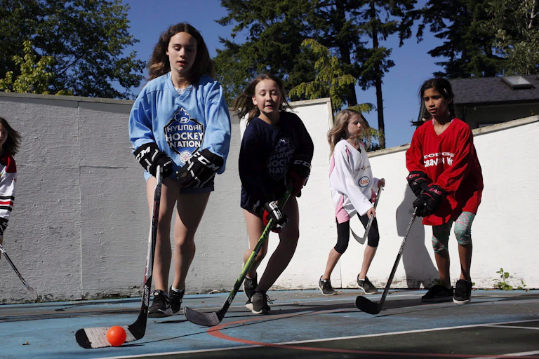 Young teen girls seen playing ballhockey outdoors.