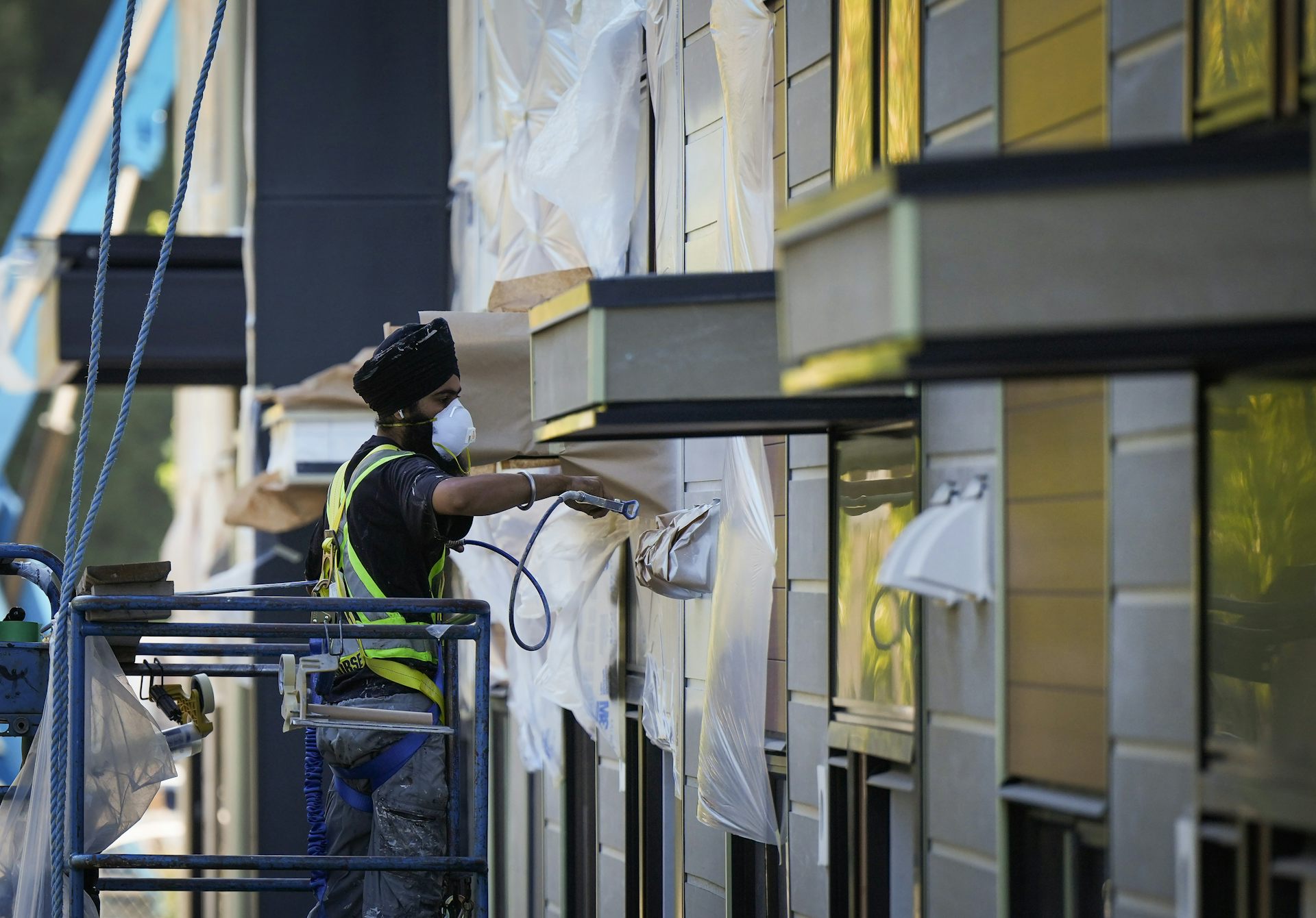 A man in a turban paints a building while on a lift.