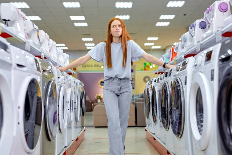 Woman standing between two rows of new washing machines in a shop.