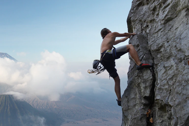 With mountains, clouds and a blue sky in the background, a young man climbs a natural rock wall.
