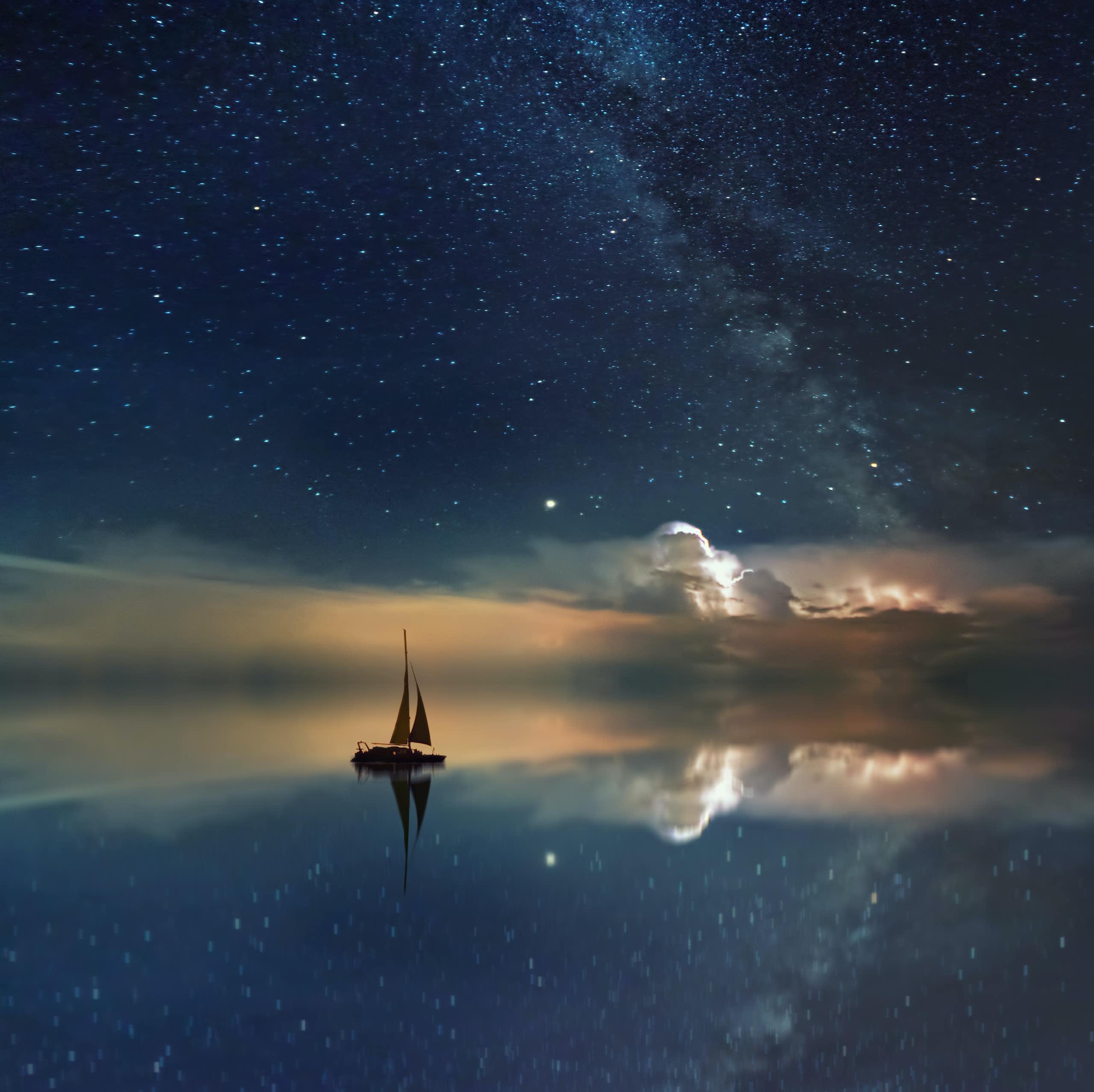 Un bateau glissant sur une mer d’huile dans laquelle se reflète le ciel étoilé