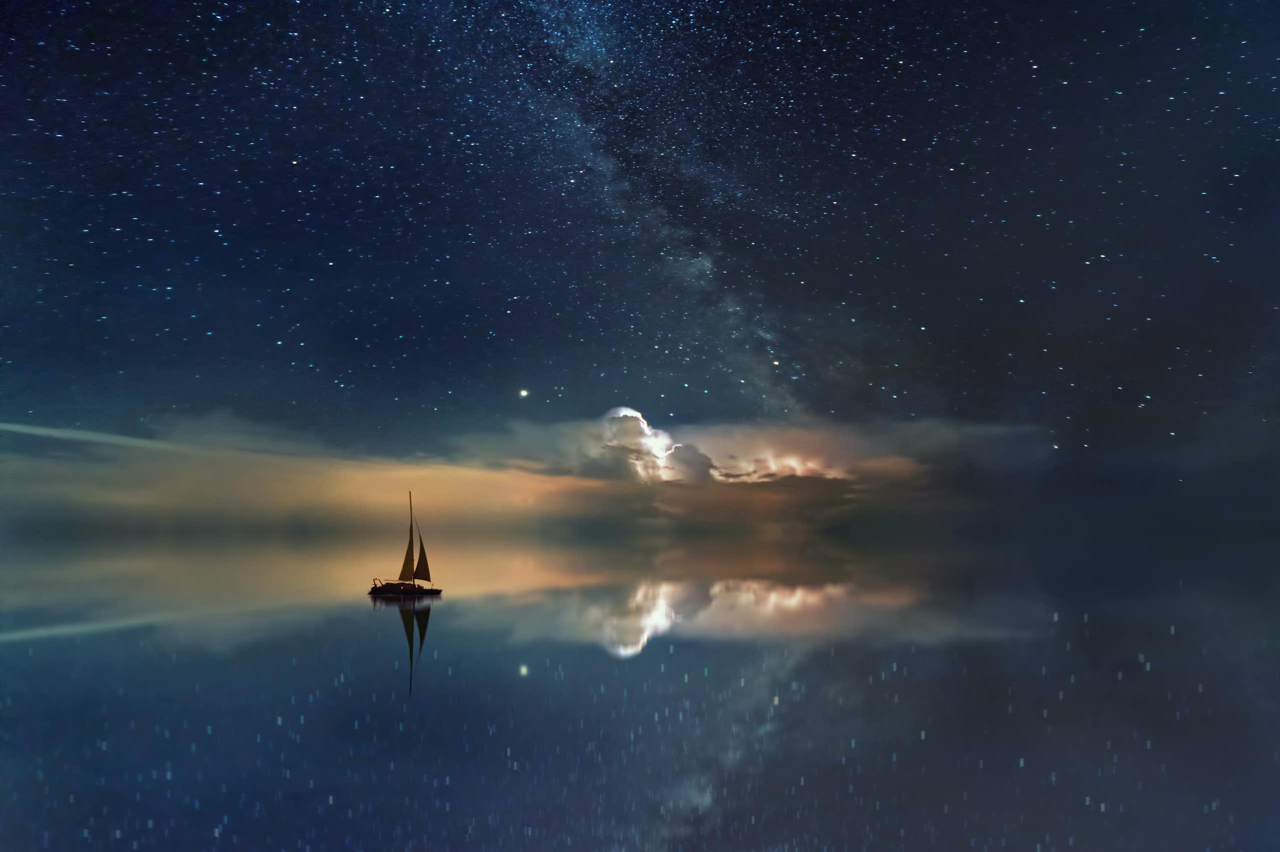 Un bateau glissant sur une mer d’huile dans laquelle se reflète le ciel étoilé