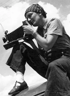 Black and white photo of Dorothea Lange taking a photo with an old-fashioned camera