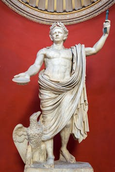 A statue of Emperor Claudius in a red-walled room.