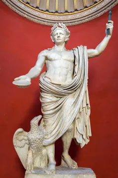 A statue of Emperor Claudius in a red-walled room.