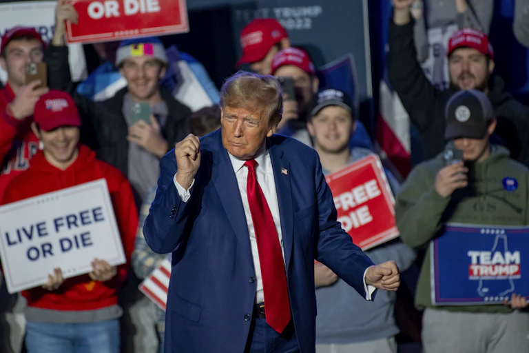 DOnald Trump surrounded by supporters with placards reading 'Live Free or Die' and 'Team Trump' December 2023.