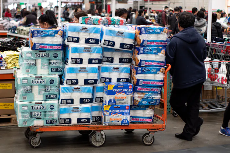 A man in a cash and carry with a trolley piled high with toilet paper.