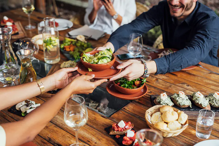 Friends passing vegetarian dishes across a crowded table.