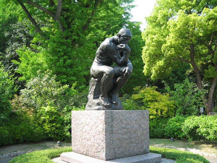 Rodin's statue The Thinker in a leafy garden.