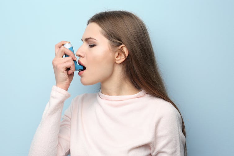 Mujer llevándose la bomba del asma a la boca