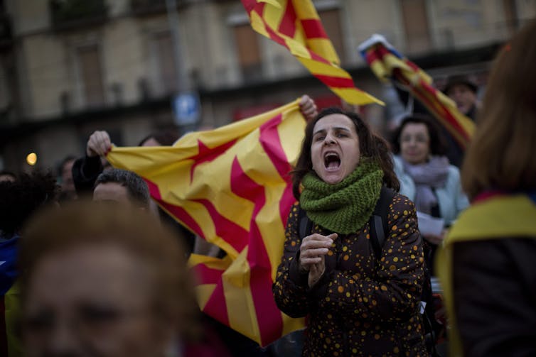 A woman shouts while people wave red and yellow flags behind her.