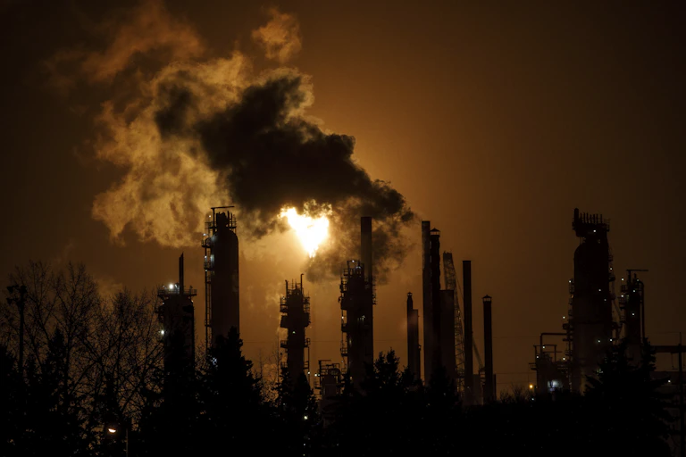 Billows of smoke pour from smokestacks with a flare behind them.